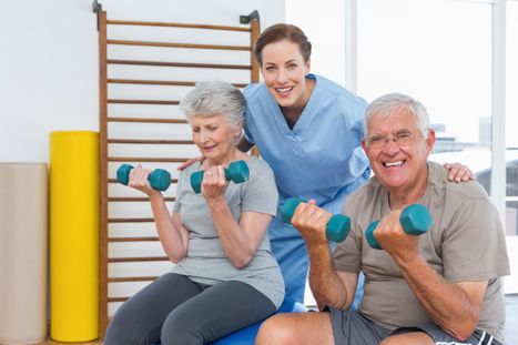 Female therapist assisting senior couple with dumbbells in the medical